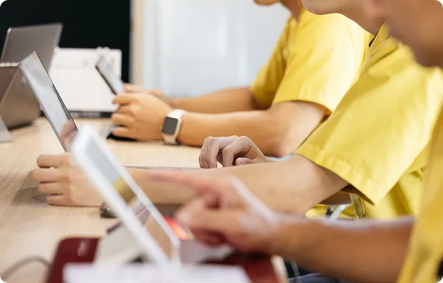 複数の参加者が並び、デジタルデバイスを操作する手元と、手首のスマートウォッチが目立つクローズアップ。