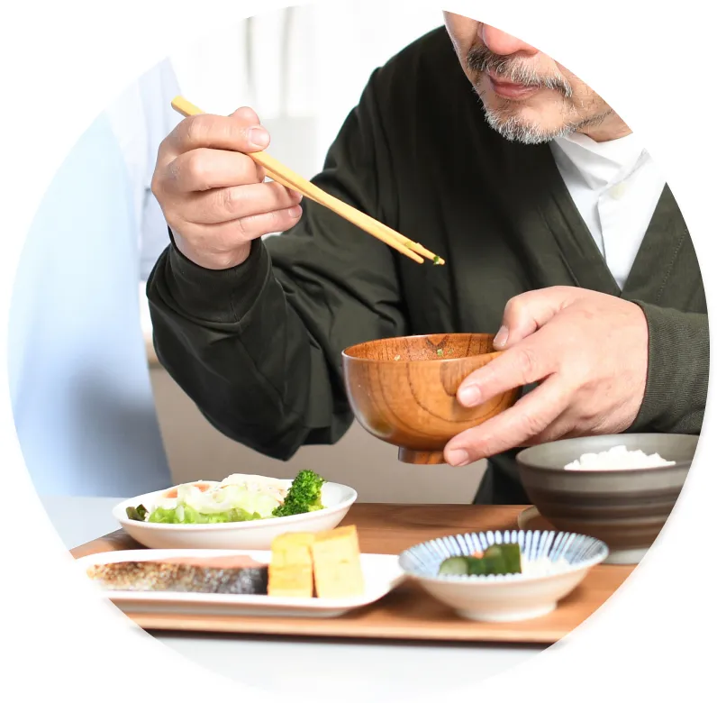 落ち着いた色合いの服を着た男性が、お膳の上の健康的な朝食を丁寧に食べている様子。