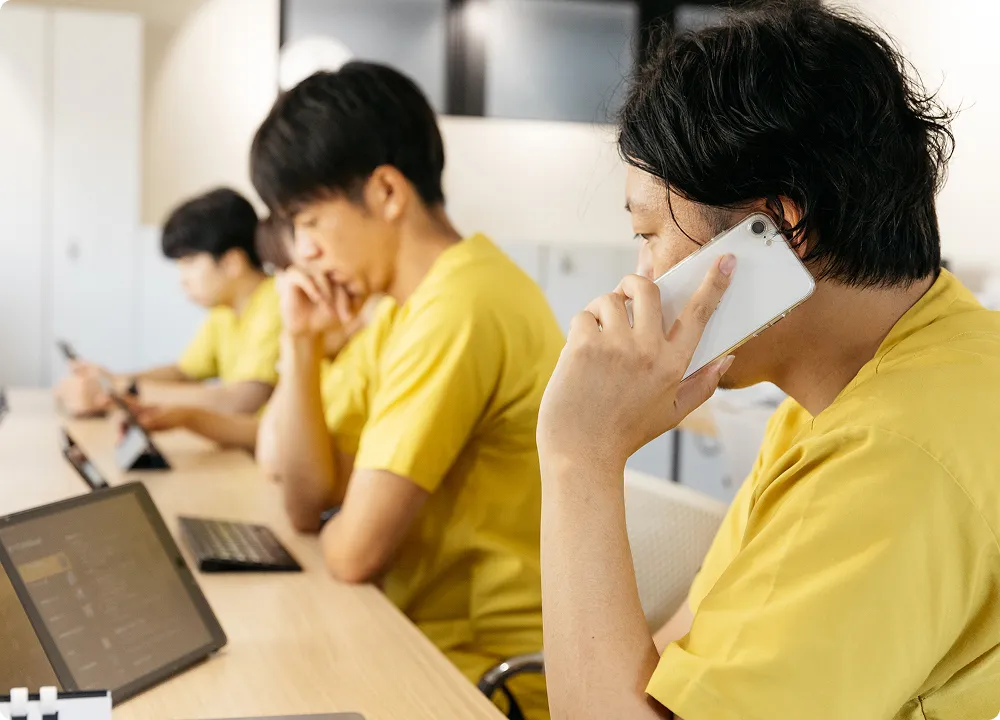 複数のスタッフが並んでデスクに向かい、タブレットや携帯電話を操作する集中した光景。