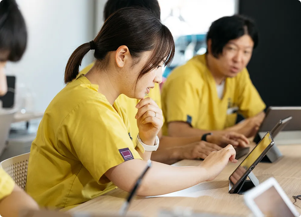 医療チームが明るい会議室でデジタルデバイスを使いながら研修を受けている横顔。