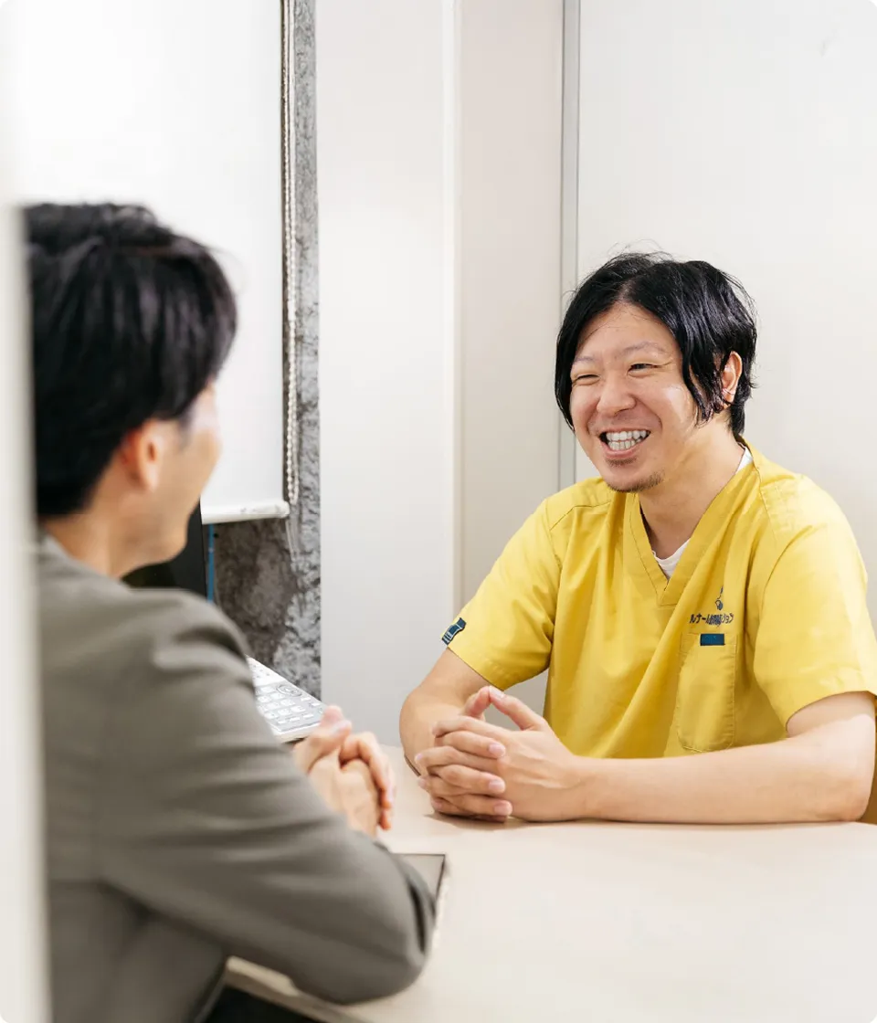 応接スペースで黄色いユニフォームのスタッフが笑顔で相談者と向き合っている様子