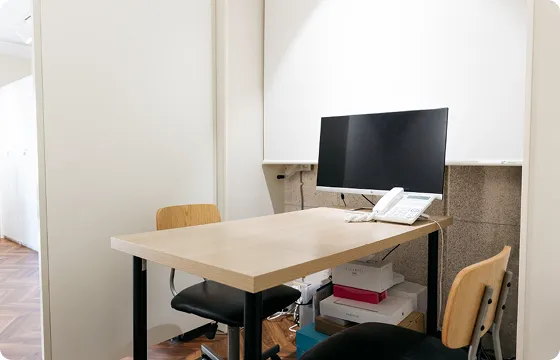 モニターと電話機が置かれたシンプルな相談室のデスクと椅子