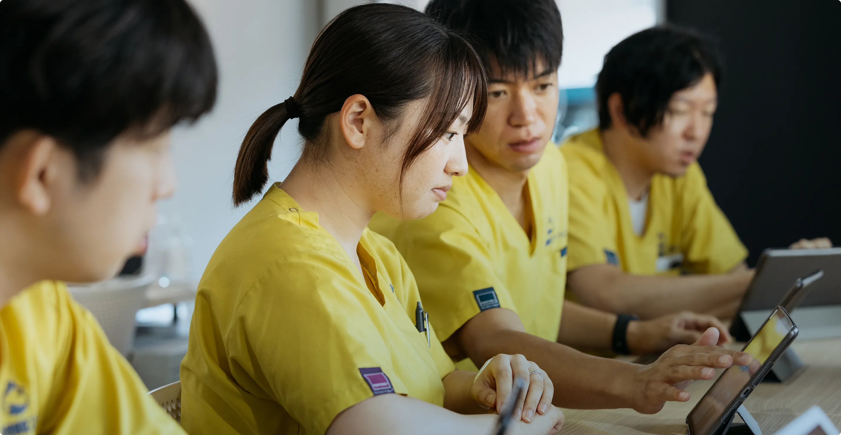 集中した表情でタブレットを操作する若者たち、チームでの知識共有の瞬間。