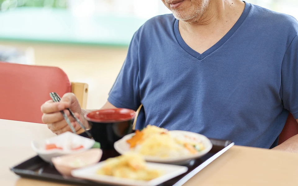 紺色のTシャツを着た男性が、食事を手に箸を持っています。